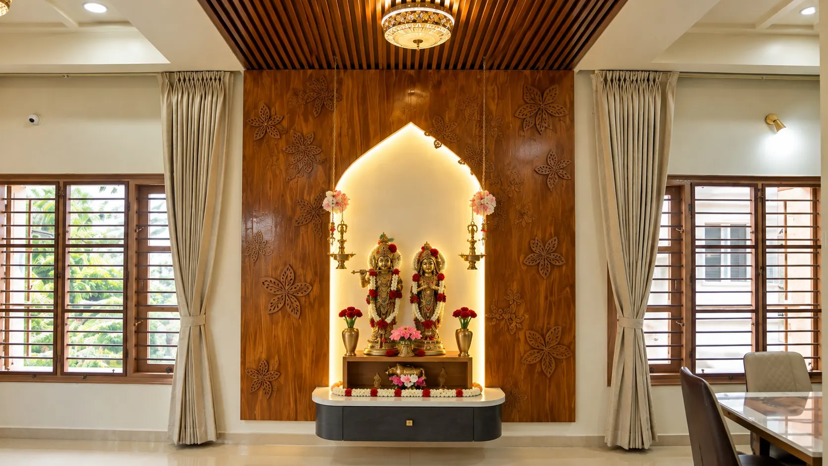 The carved timber pooja wall with its lit arch, framed by curtained windows
