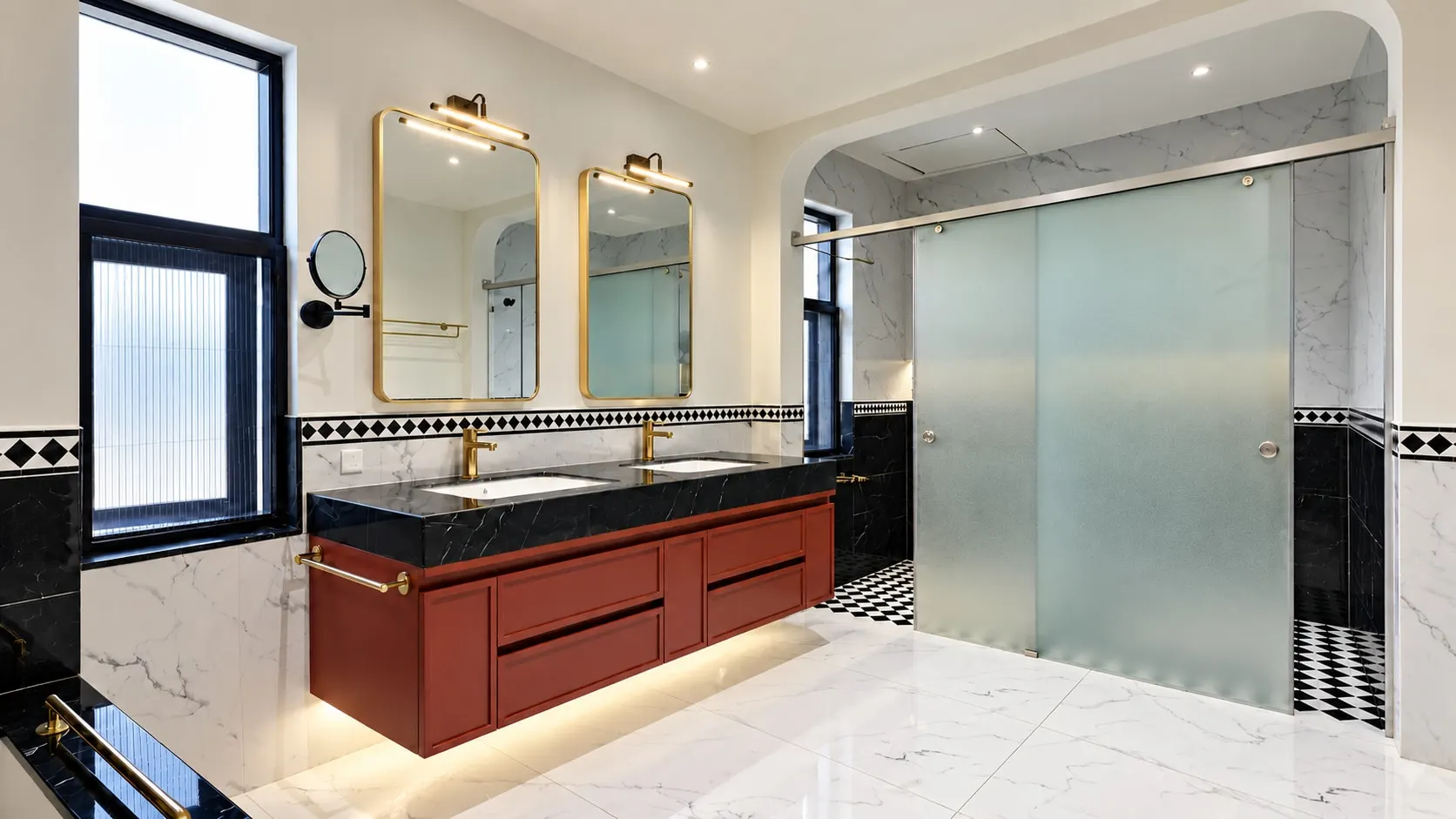 Bathroom with a red twin-basin vanity under black marble, brass-framed mirrors, marble walls and a frosted glass shower