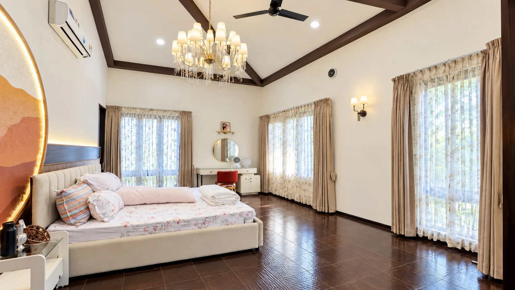 Main bedroom under a pitched ceiling with dark timber beams, a crystal chandelier, an upholstered bed and tall curtained windows