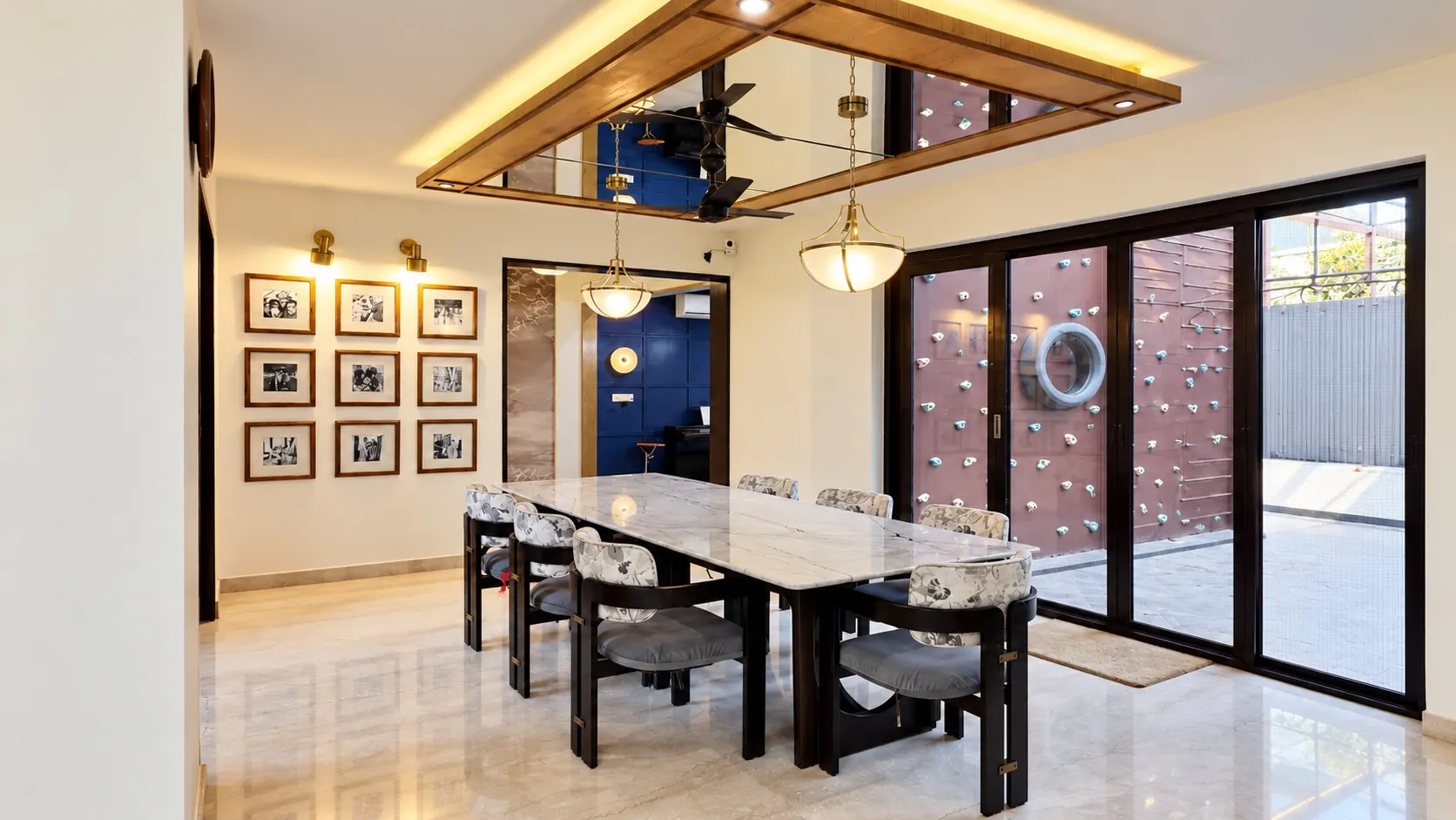 Dining room with a marble-top table, a mirrored timber ceiling frame with pendant lights, a gallery wall of black-and-white photographs and glass doors to a courtyard