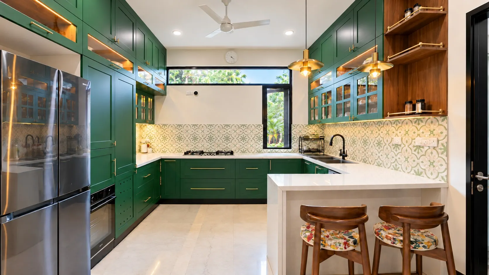 Emerald-green kitchen with brass handles, patterned wall tiles, open timber shelves and a white breakfast counter with two stools