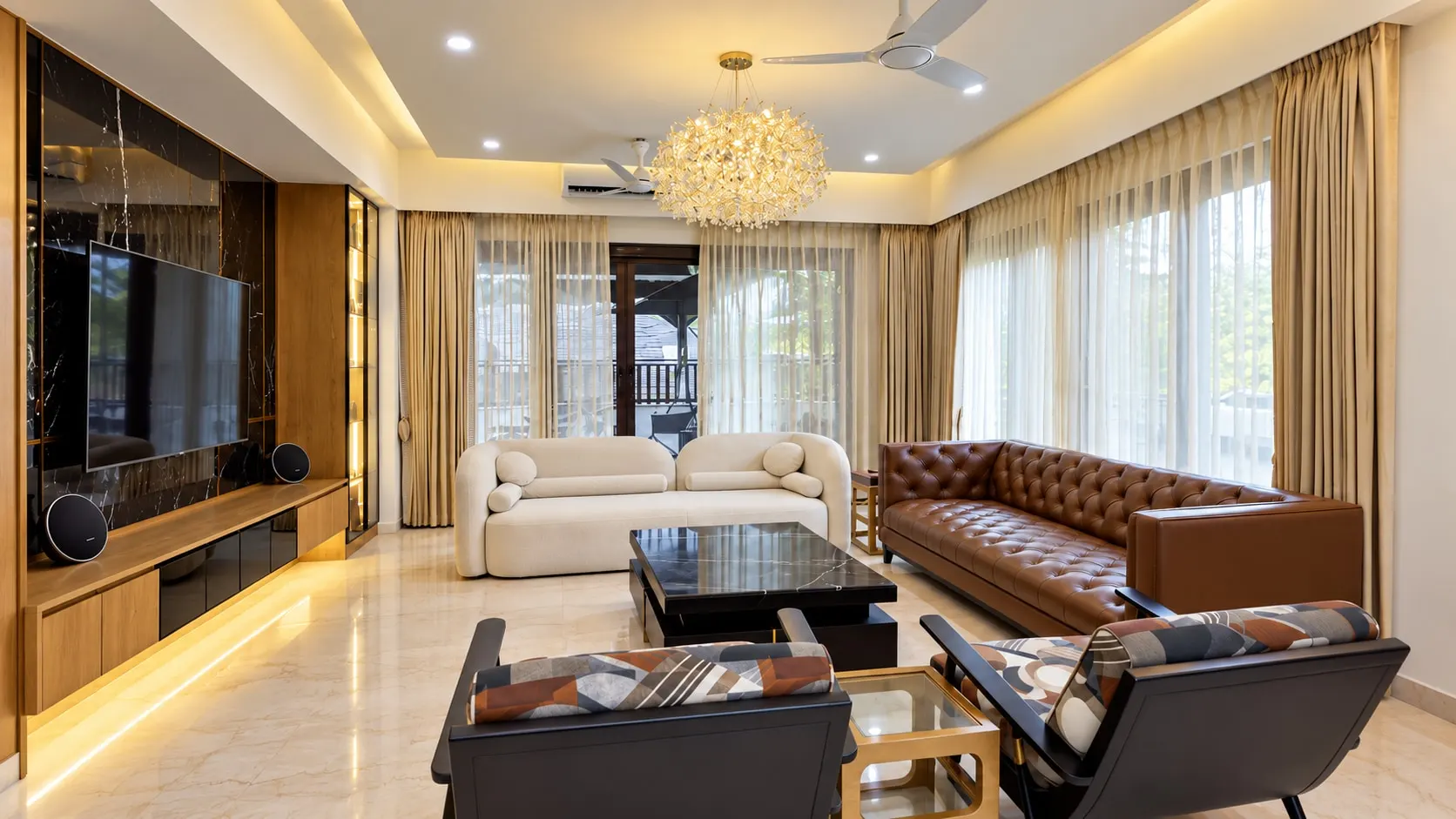 Living room with a black marble television wall lit from below, a crystal chandelier, a white sofa and a tan leather Chesterfield