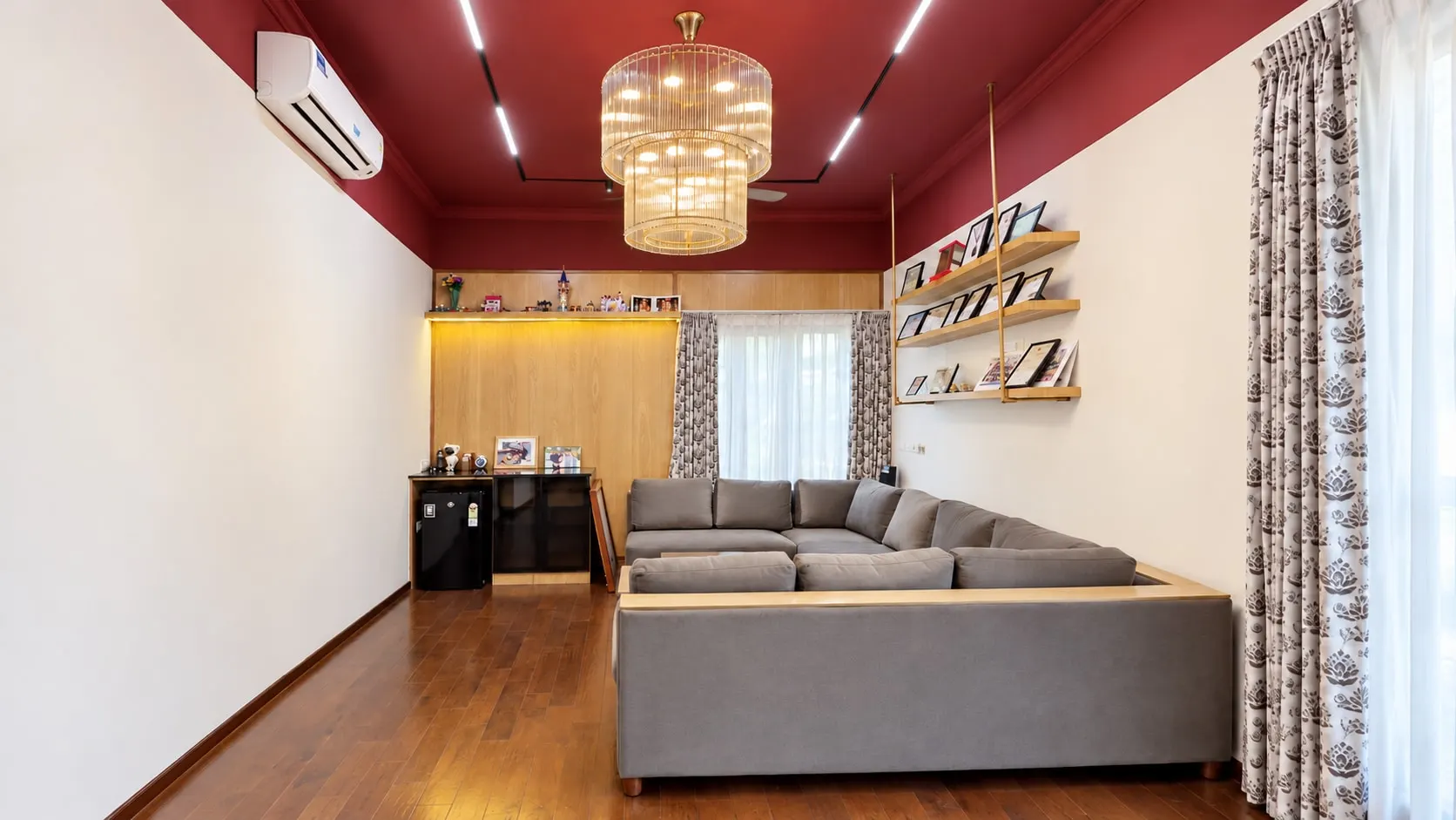 Family lounge with a deep red ceiling and linear lights, a tiered glass chandelier, a grey L-shaped sofa and display shelves