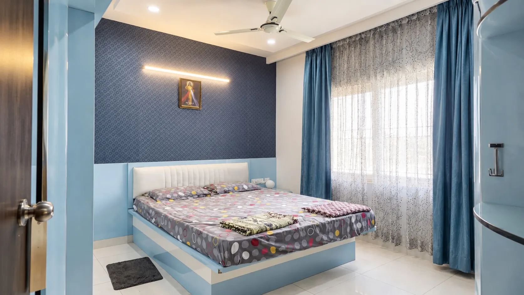 Bedroom with a navy patterned wall above sky-blue panelling, a white upholstered headboard and blue curtains