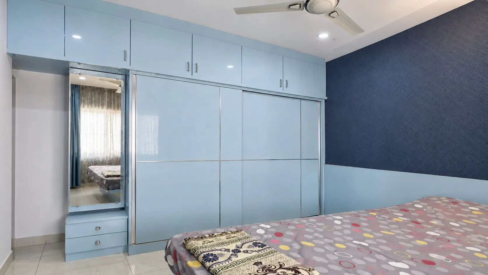 Full-height sky-blue gloss wardrobe with a mirror and drawers, beside a navy patterned wall