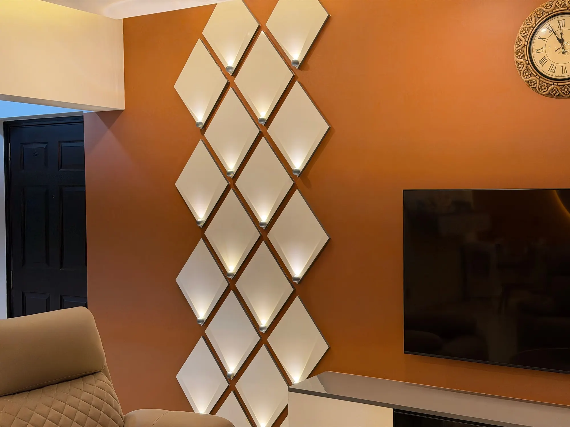 Close view of the lit panel of white diamonds on the burnt-orange wall beside the television