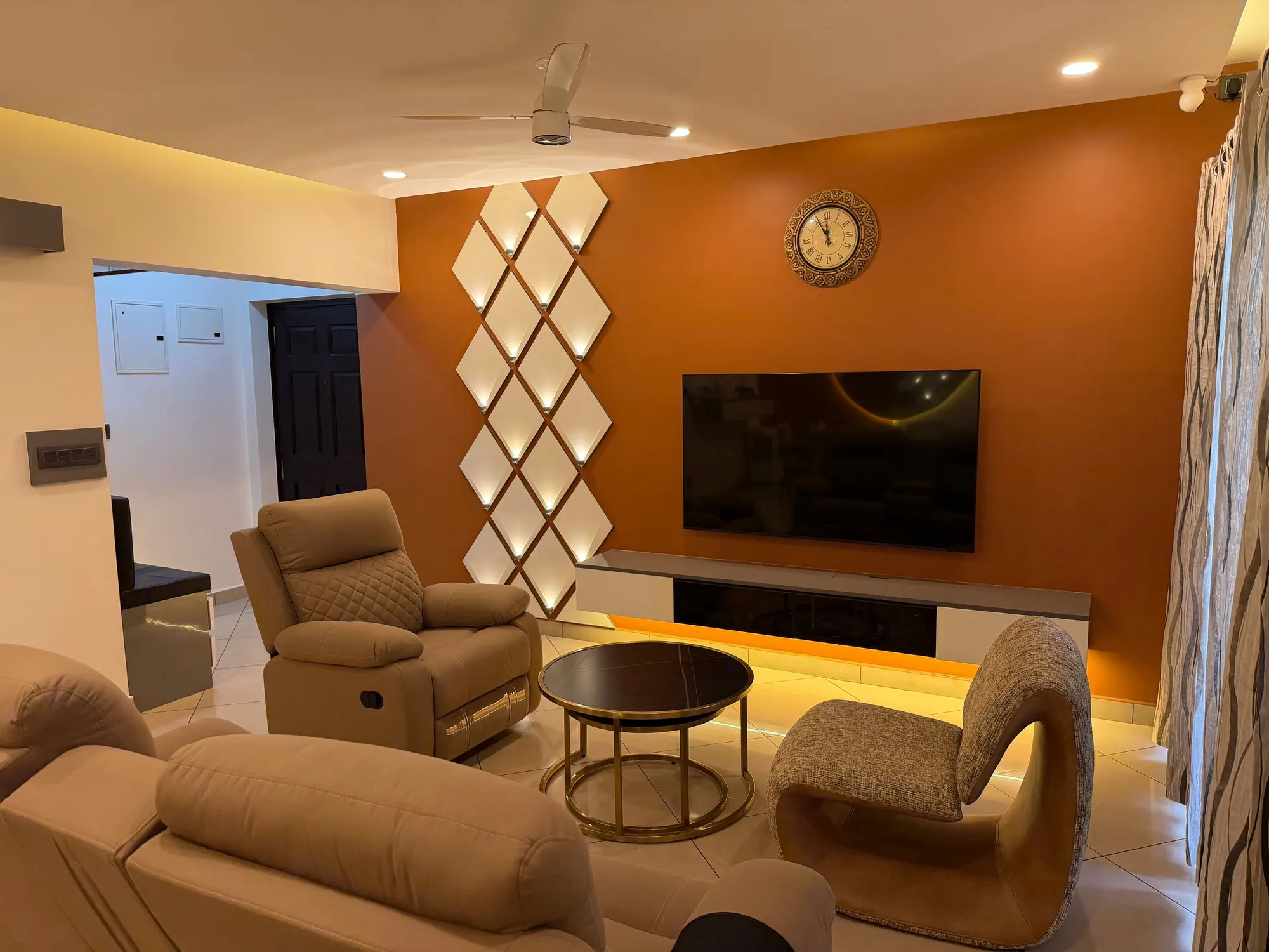 Living room with a burnt-orange TV wall, a lit panel of white diamonds, a wall clock, recliners and a brass-ringed coffee table