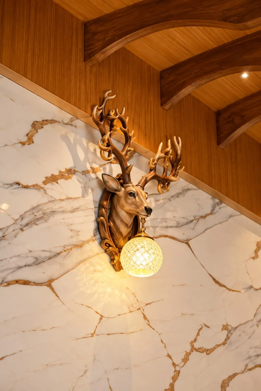 A deer-head wall lamp holding a crystal globe, on a marble-finish wall beneath curved timber beams