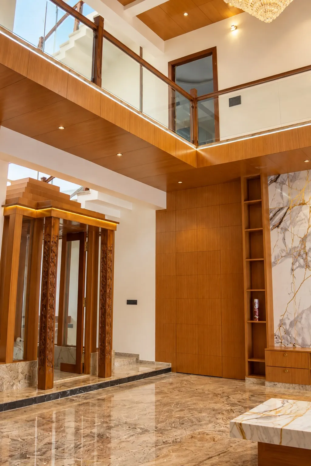 The hall beneath a gallery with glass railings: a timber pavilion on carved pillars, timber wall panelling and tall display shelves