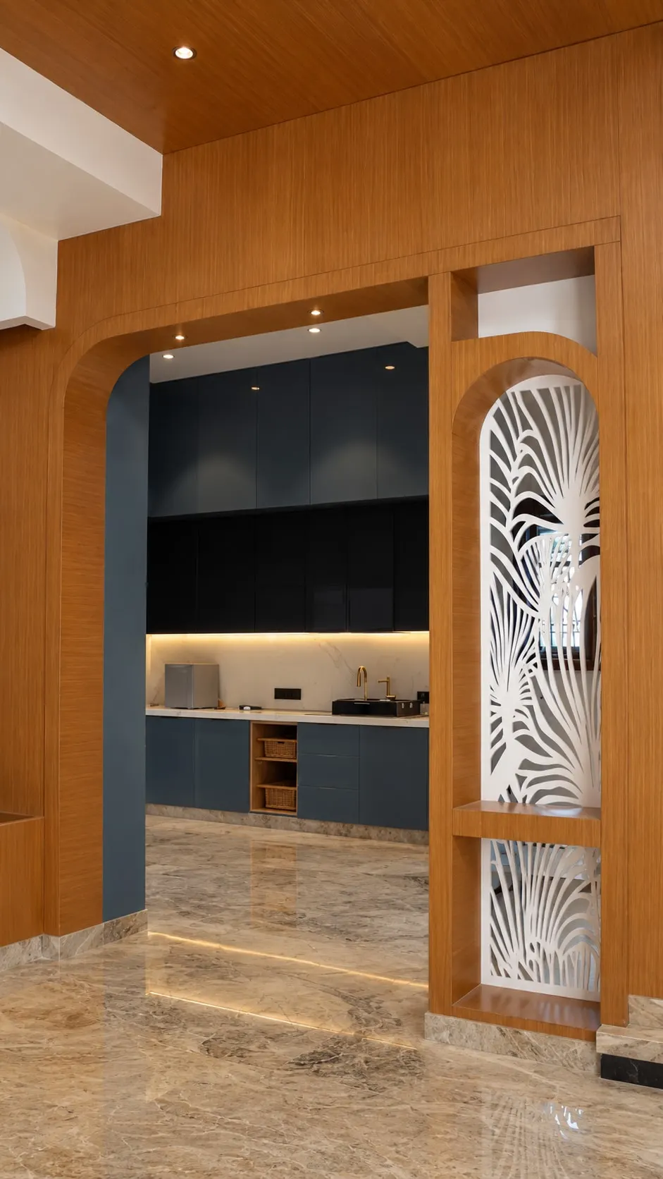 Navy kitchen with under-cabinet lighting, seen through a timber arch beside a laser-cut leaf screen