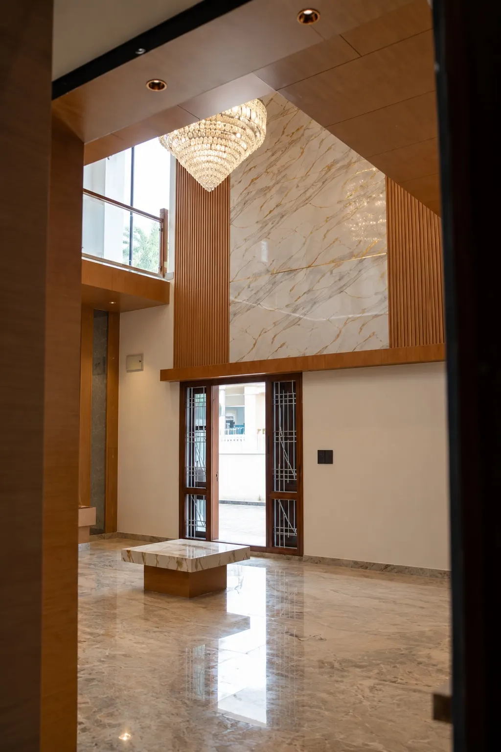 Double-height living room with a crystal chandelier, a marble-finish feature wall between timber slats, and a polished marble floor