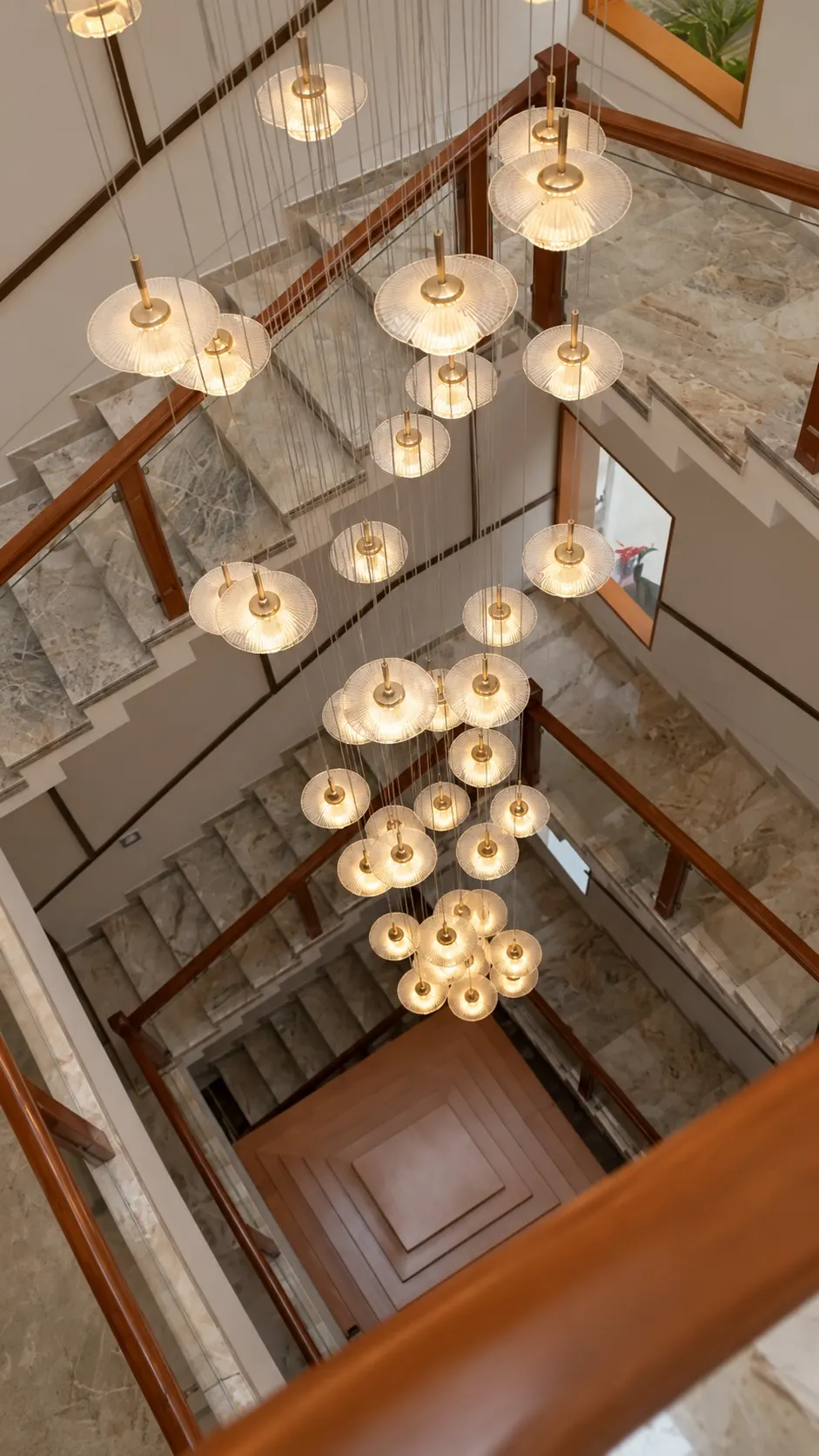 Looking down the stairwell: clusters of glass pendant lights hanging through the marble stairs and timber handrails
