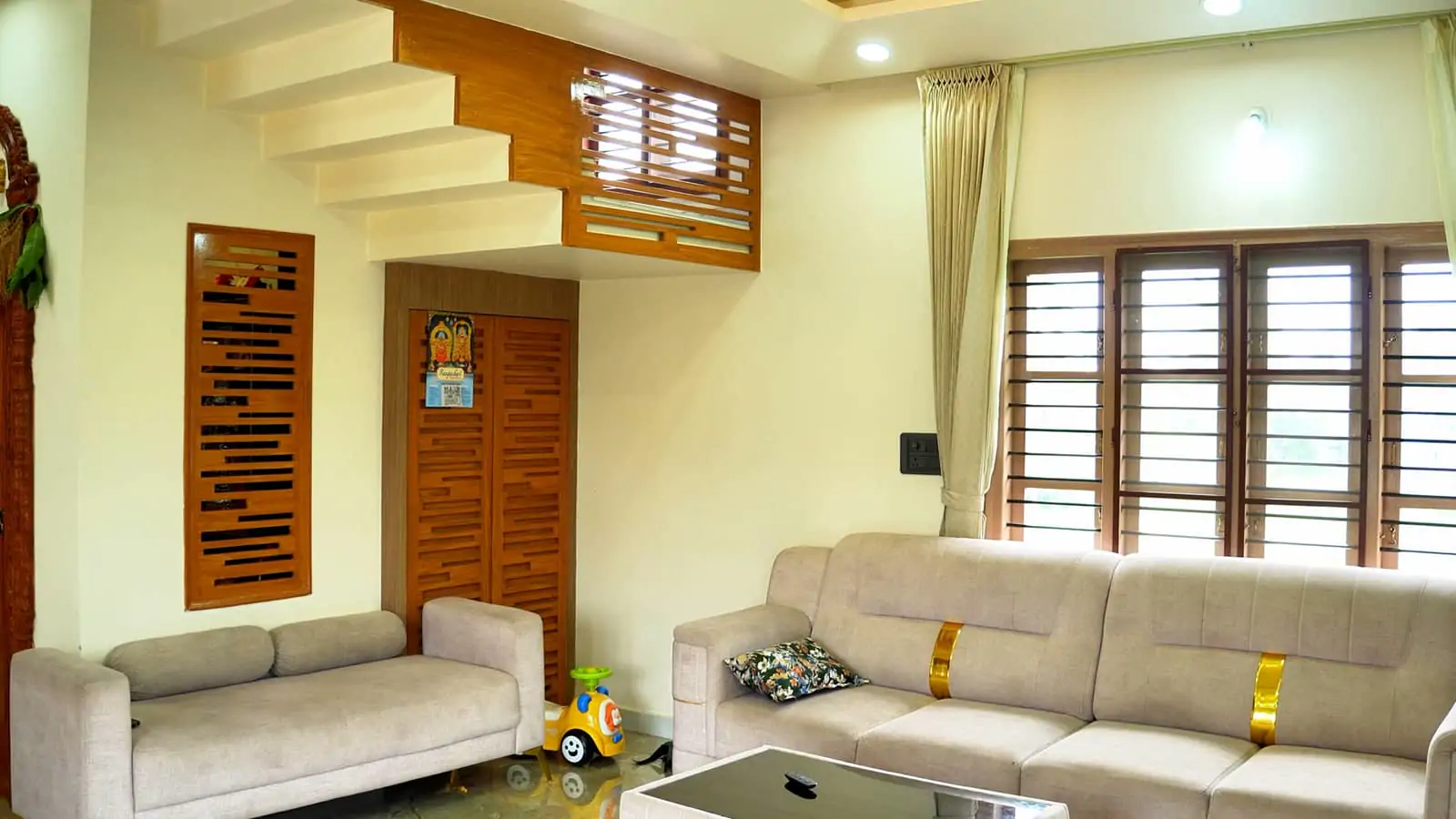 A living room in a completed home: a low sofa, a timber staircase, carved doors and shuttered windows