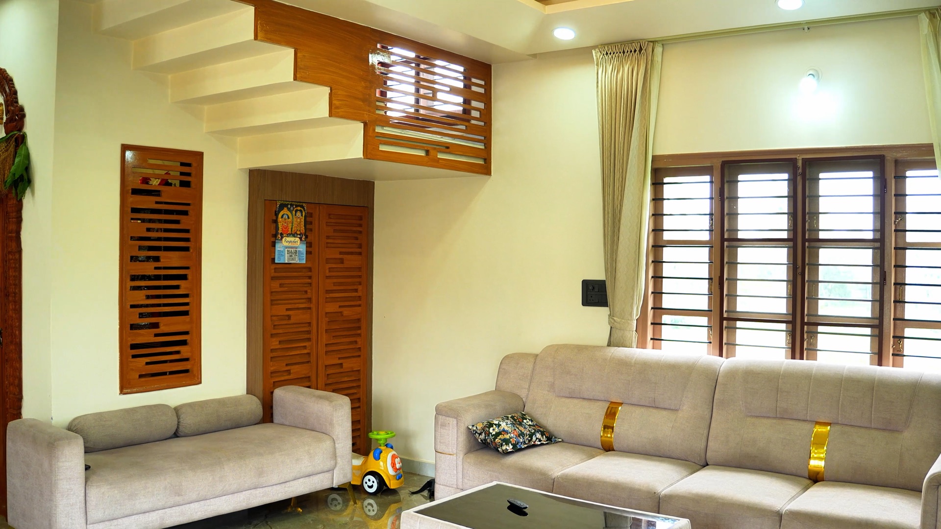 A living room in a completed home: a low sofa, a timber staircase, carved doors and shuttered windows